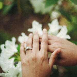 Intimate close-up of a hand with an engagement ring resting on white flowers outdoors.