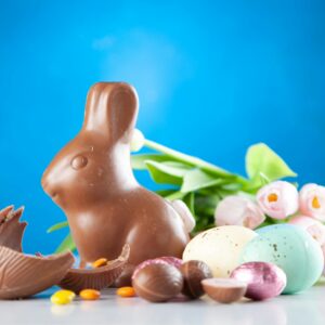 A delightful Easter scene with a chocolate bunny, colorful eggs, and pink tulips on a blue background.