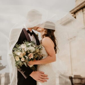 Bride and groom share a tender kiss under a veil, showcasing love and romance on their special day.