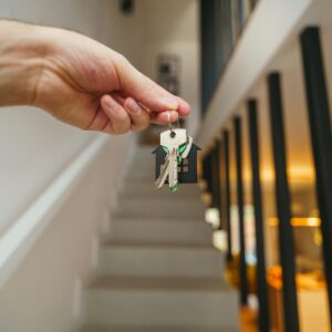 A hand holding house keys in a modern interior, symbolizing new home ownership or real estate investment.