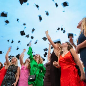 Group of graduates celebrating by tossing caps in the air against a bright sky.